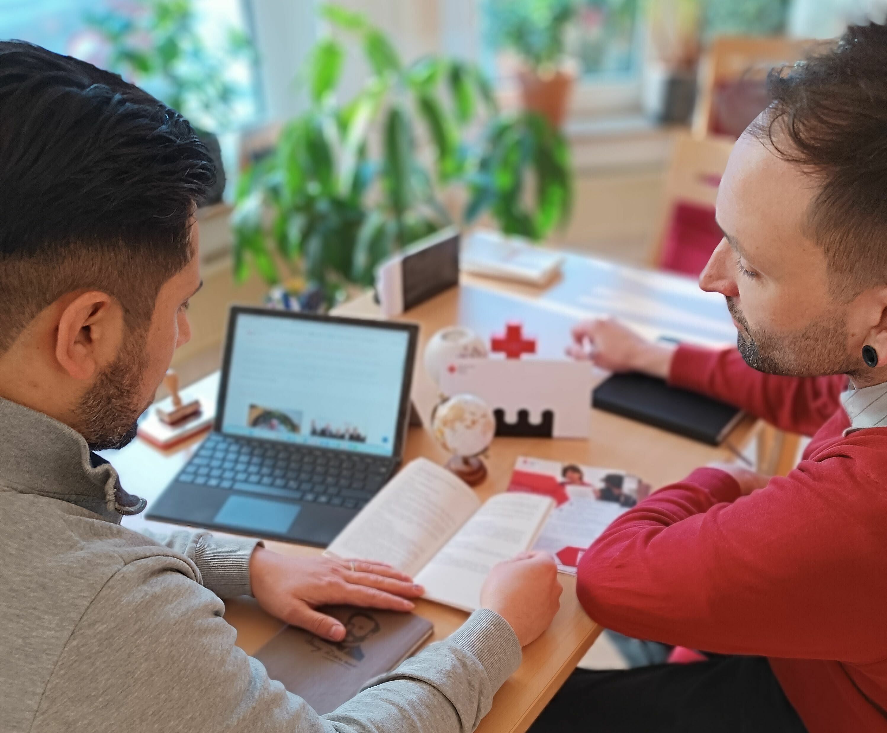 Zwei Männer sitzen am Tisch mit Laptop und Beratungsflyern