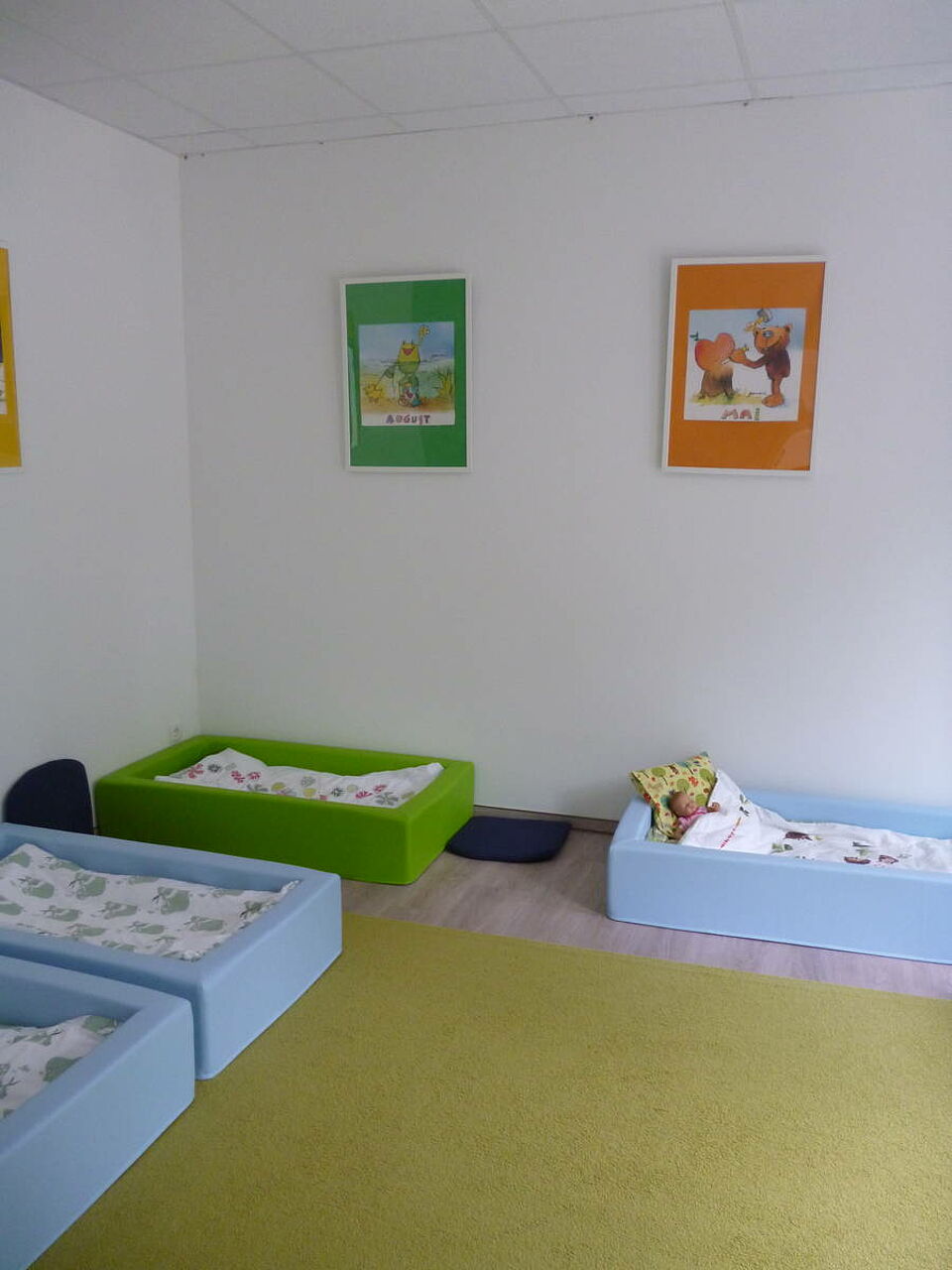 Rothemühler Knirpse_Schlagraum Schlafraum mit kleinen bodentiefen Betten für die Kinder. An der Wand hängen bunte Bilder