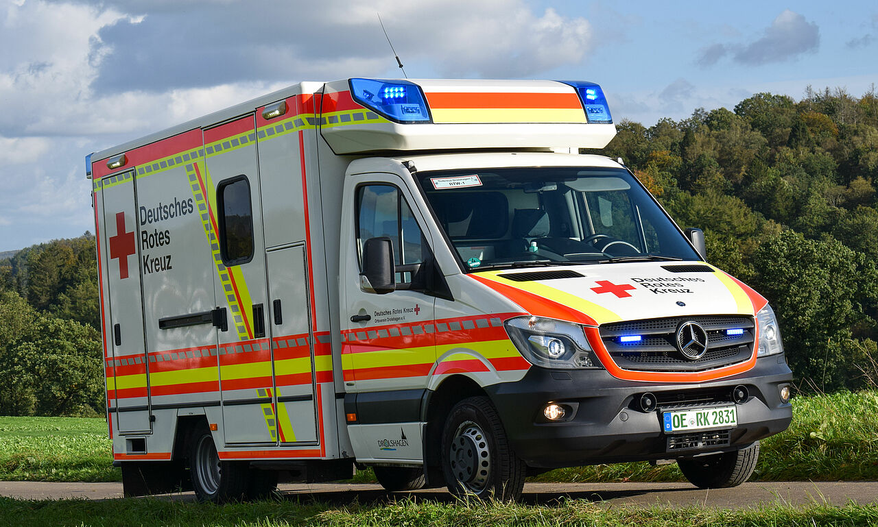 Bühnenbild_DRK-OV-Drolshagen Rettungswagen fährt an einem sonnigen Tag zwischen den Feldern