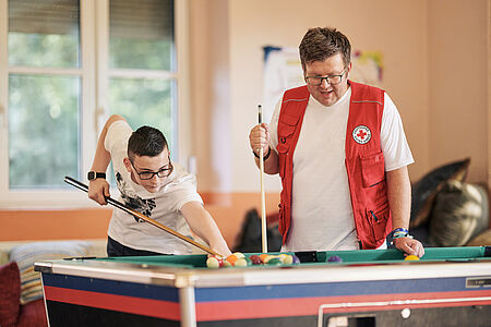 DRK-Jugenhilfe Ein Mitarbeitender des DRK mit DRK-Kleidung spielt mit einem Jugendlichen Billiard